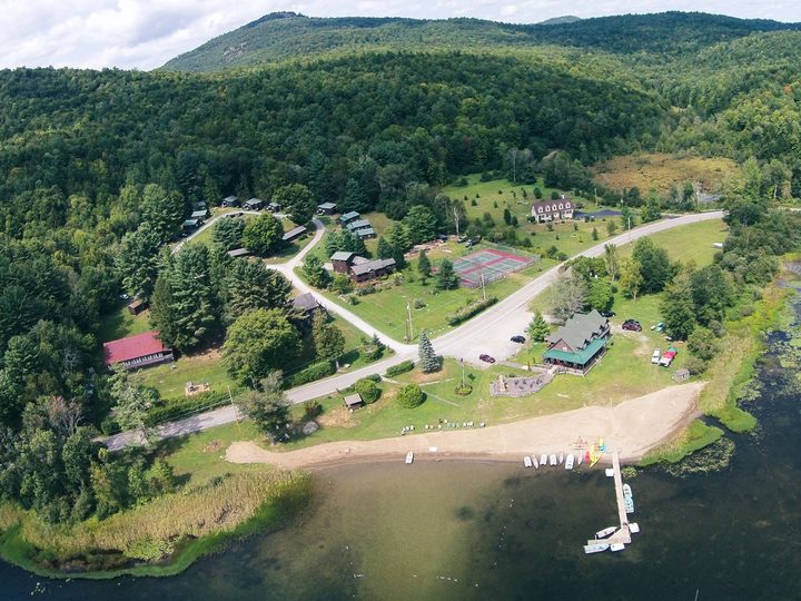 Aerial view of Twin Pines on Trout Lake: the sandy beach, dock and boats in front of the lodge, with the cottages and tennis courts set among the pines