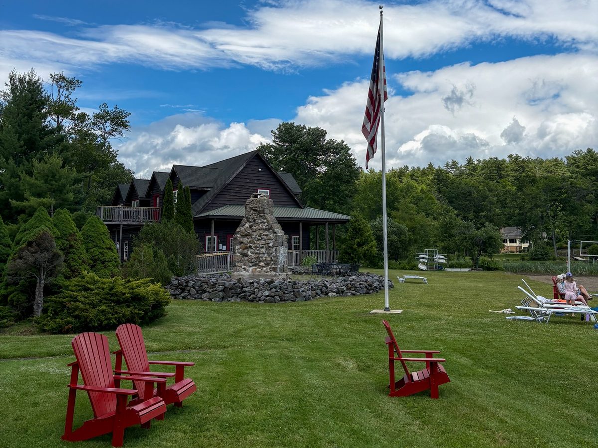 Red Adirondack chairs on the lawn at Twin Pines, with the stone chimney, the flag and the lodge under a blue summer sky