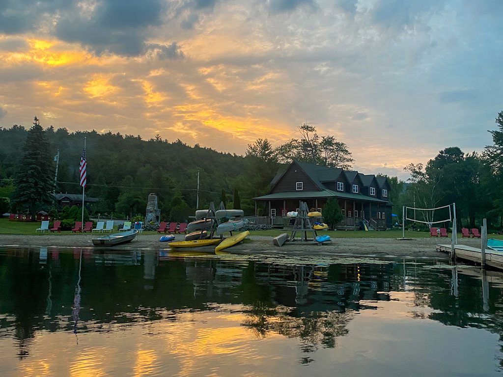 The Twin Pines beach at sunset seen from Trout Lake, with kayaks, canoes and a rowboat on the sand